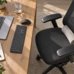 Blat biurka z klawiaturą, myszą, szklanką wody oraz ergonomicznym fotelem z podparciem lędźwiowym